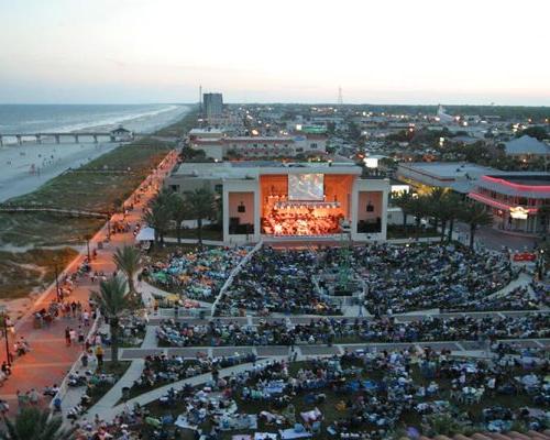 Birds-eye view of large crowd gathered around the Sea Walk Pavilion listening to a concert at dusk.